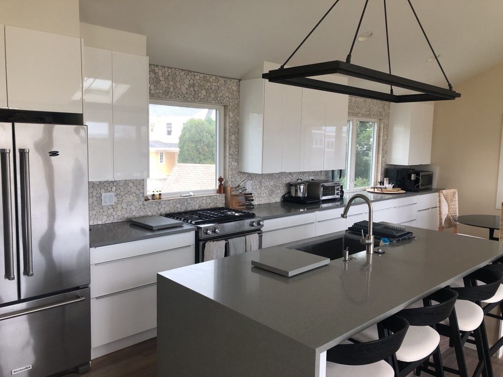 modern kitchen with gray and white fixtures, including a gray island with white seats and a black hanging lamp